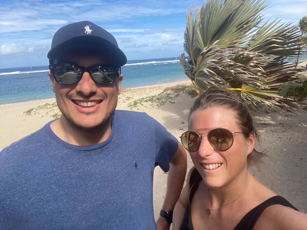 Fabien et Pamela souriants sur une plage de La Réunion, ciel bleu et cocotier.
